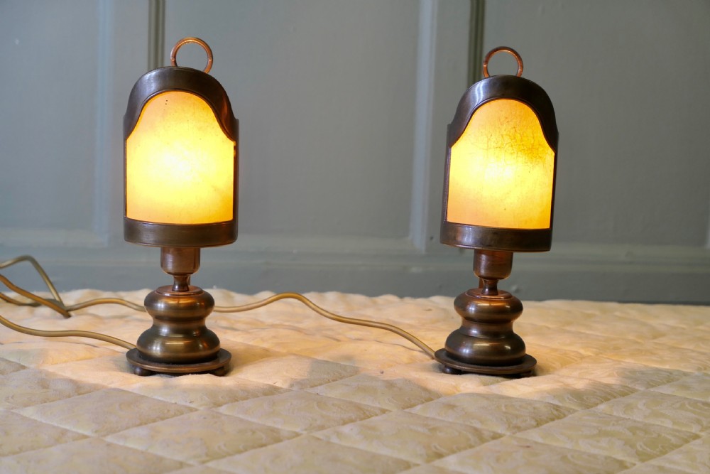 A pair of turned brass bedside lamps with railway lantern styled cowls, ring finials, and illuminated amber parchment shades. View II