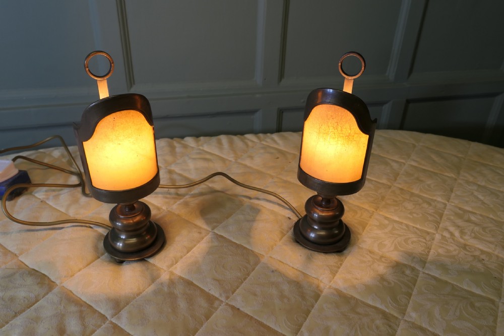 A pair of turned brass bedside lamps with railway lantern styled cowls, ring finials, and illuminated amber parchment shades. View VIII