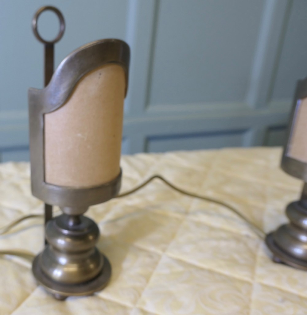 A pair of turned brass bedside lamps with railway lantern styled cowls, ring finials, and illuminated amber parchment shades. View X