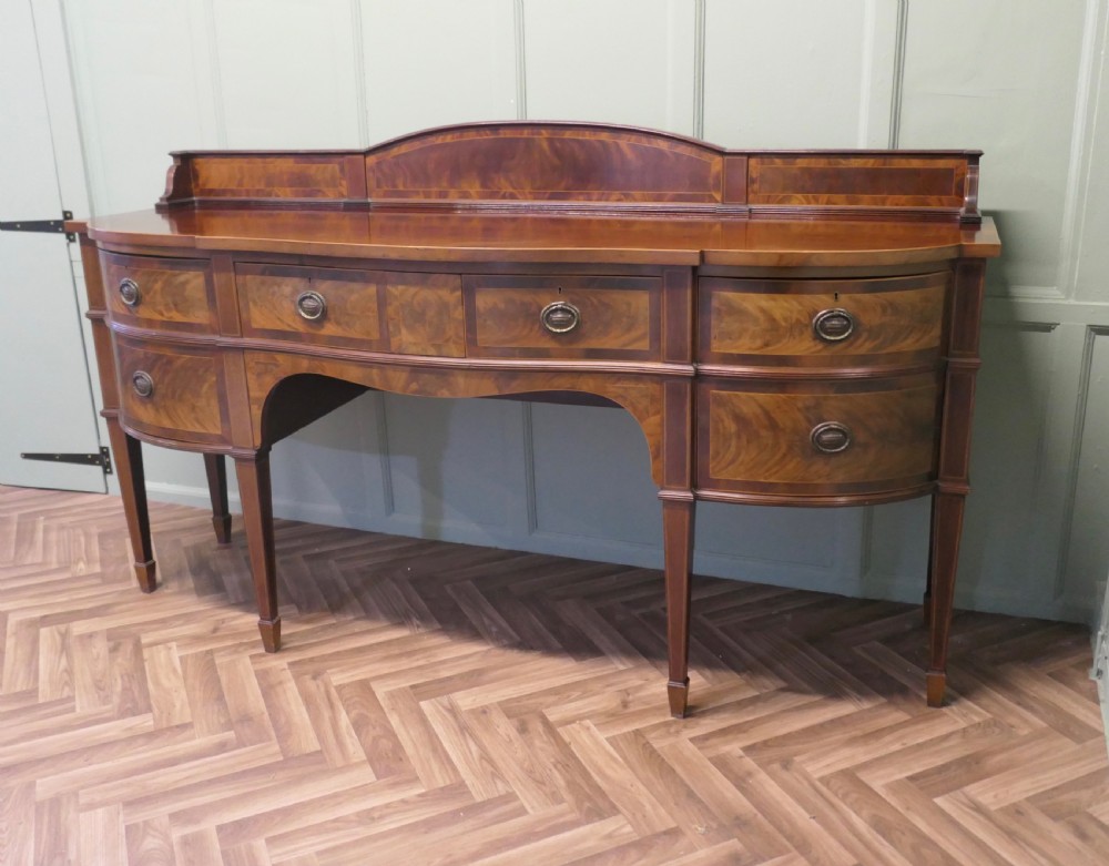 A 19th-century mahogany bow-fronted sideboard featuring flame veneer drawer fronts, brass drop ring handles, a raised upstand, and tapered square legs. View II