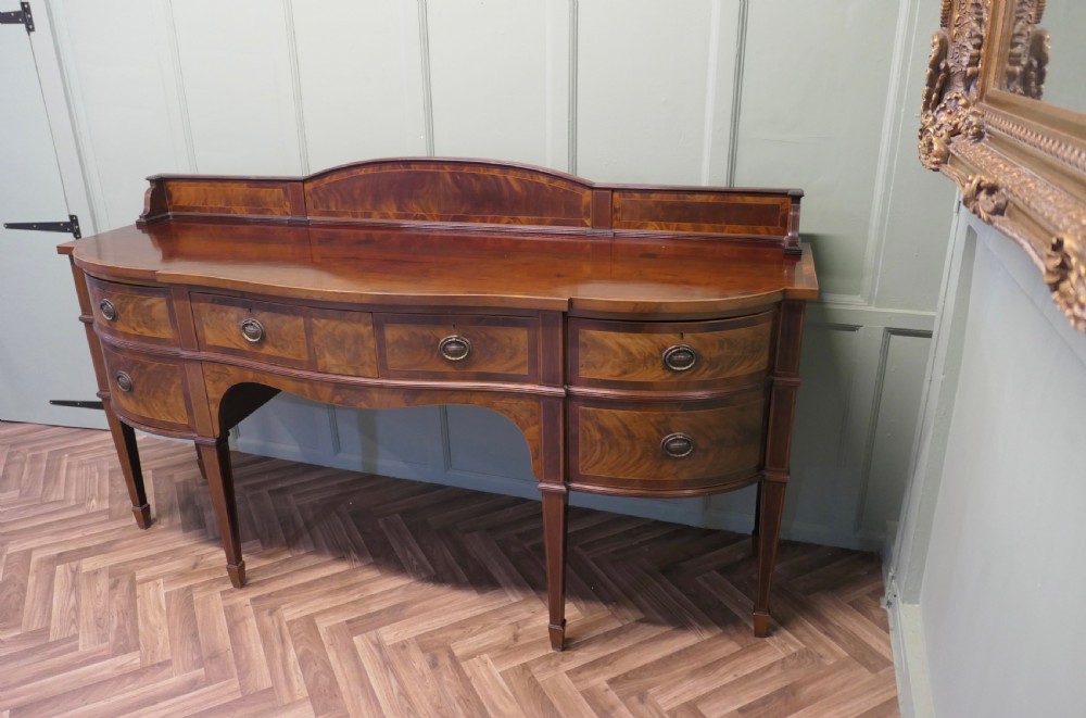 A 19th-century mahogany bow-fronted sideboard featuring flame veneer drawer fronts, brass drop ring handles, a raised upstand, and tapered square legs. View III