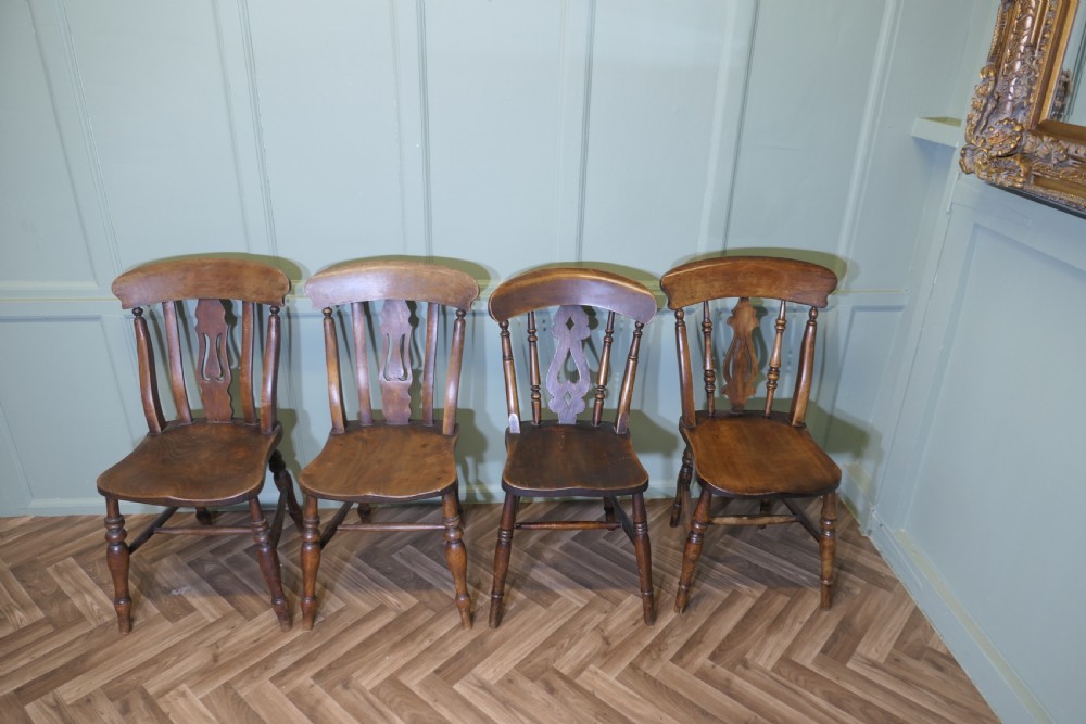 A harlequin set of four antique beech and elm dining chairs featuring shaped fiddle back splats, spindle supports, shaped wooden seats, and turned front legs.