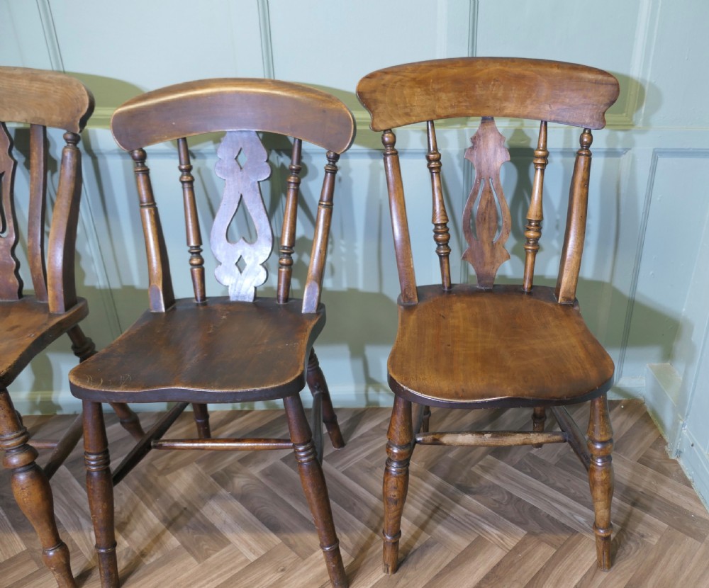A harlequin set of four antique beech and elm dining chairs featuring shaped fiddle back splats, spindle supports, shaped wooden seats, and turned front legs. View III