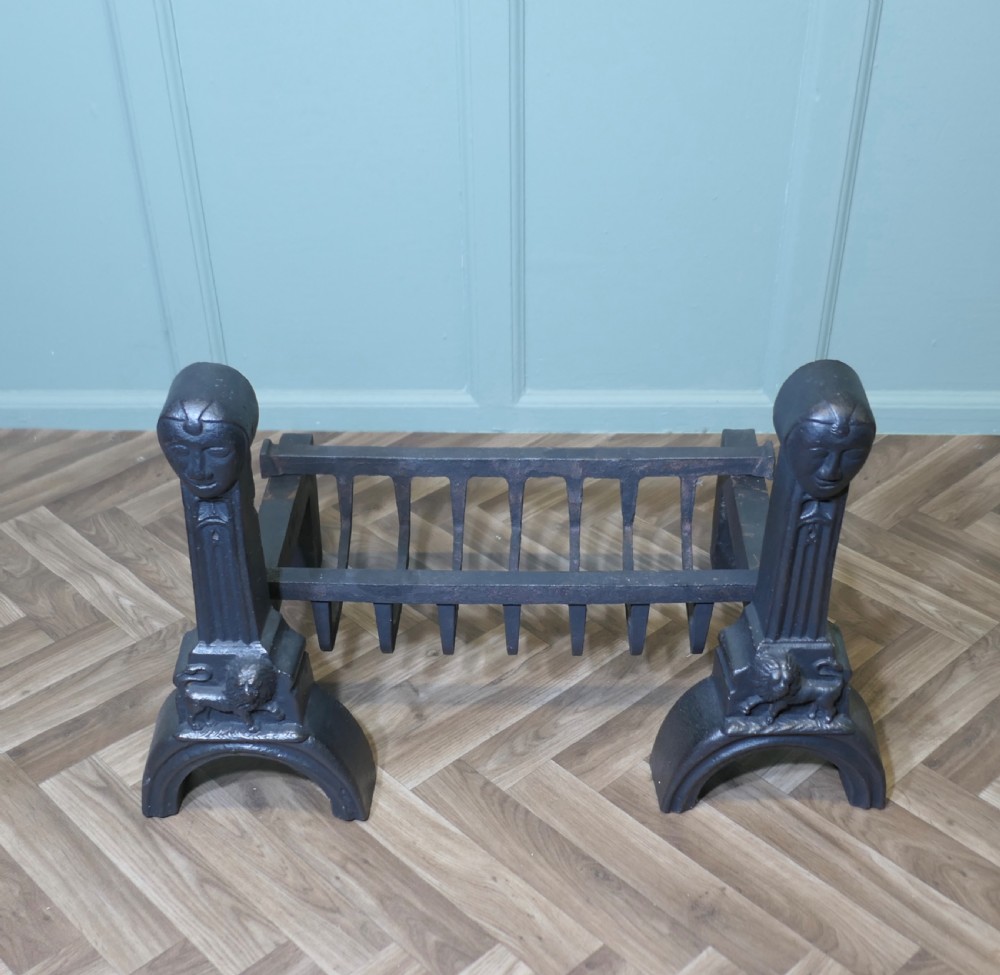 A heavy black cast iron inglenook fire grate supported by two ornate firedogs featuring sculpted relief heads and lion bases. View II
