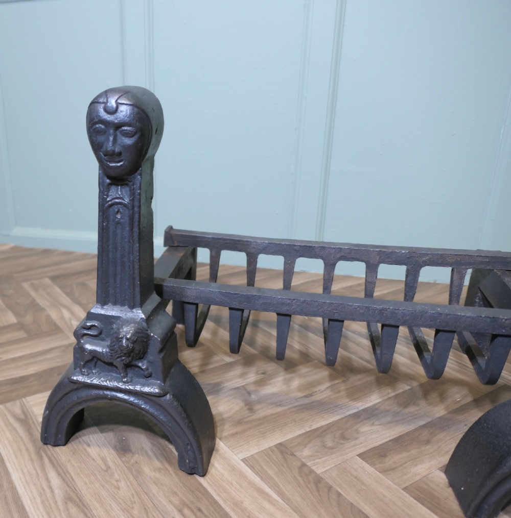 A heavy black cast iron inglenook fire grate supported by two ornate firedogs featuring sculpted relief heads and lion bases. View III