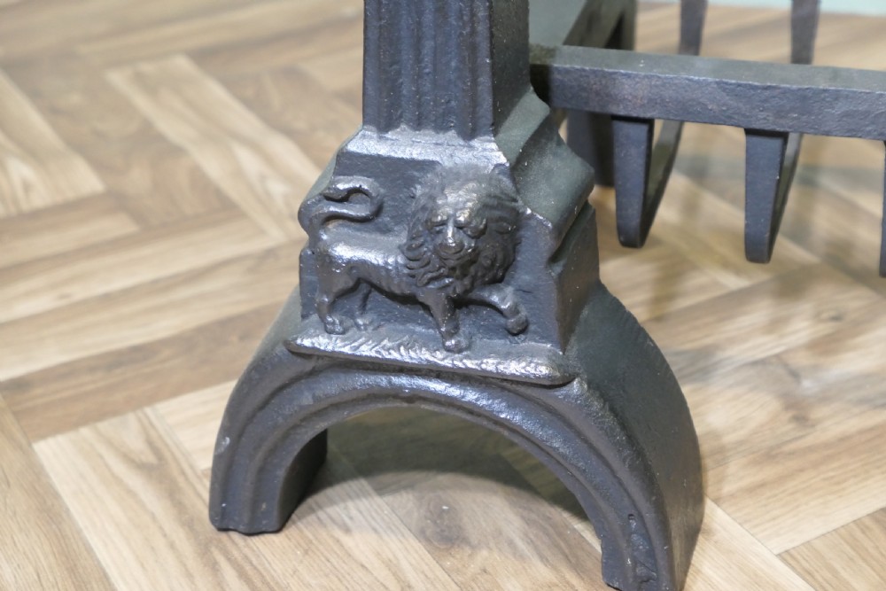 A heavy black cast iron inglenook fire grate supported by two ornate firedogs featuring sculpted relief heads and lion bases. View V