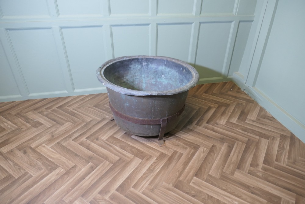 A large round patinated copper vessel with a rolled rim resting inside a dark wrought iron stand. View II
