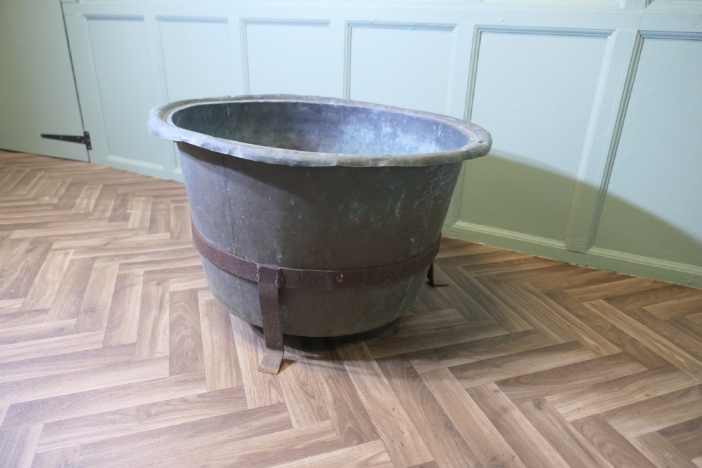 A large round patinated copper vessel with a rolled rim resting inside a dark wrought iron stand. View III