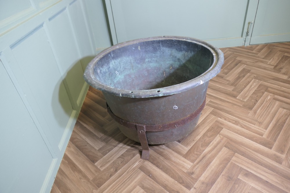 A large round patinated copper vessel with a rolled rim resting inside a dark wrought iron stand. View V