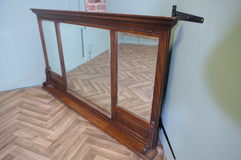 A wide dark oak overmantel frame featuring three rectangular glass mirror panels with carved moulding details along the top frieze and lower edge. View VI