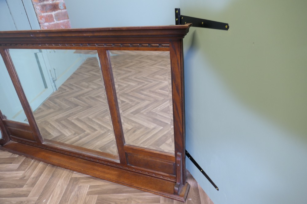 A wide dark oak overmantel frame featuring three rectangular glass mirror panels with carved moulding details along the top frieze and lower edge. View VII