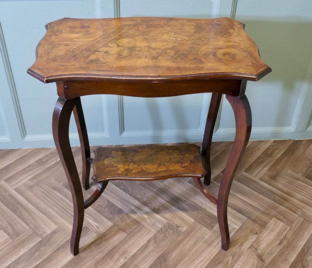 A warm brown wooden occasional table featuring a shaped serpentine top with central floral decoration, slender cabriole legs, and a decorated lower shelf.