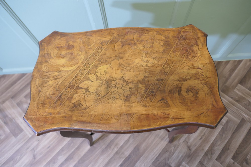 A warm brown wooden occasional table featuring a shaped serpentine top with central floral decoration, slender cabriole legs, and a decorated lower shelf. View V
