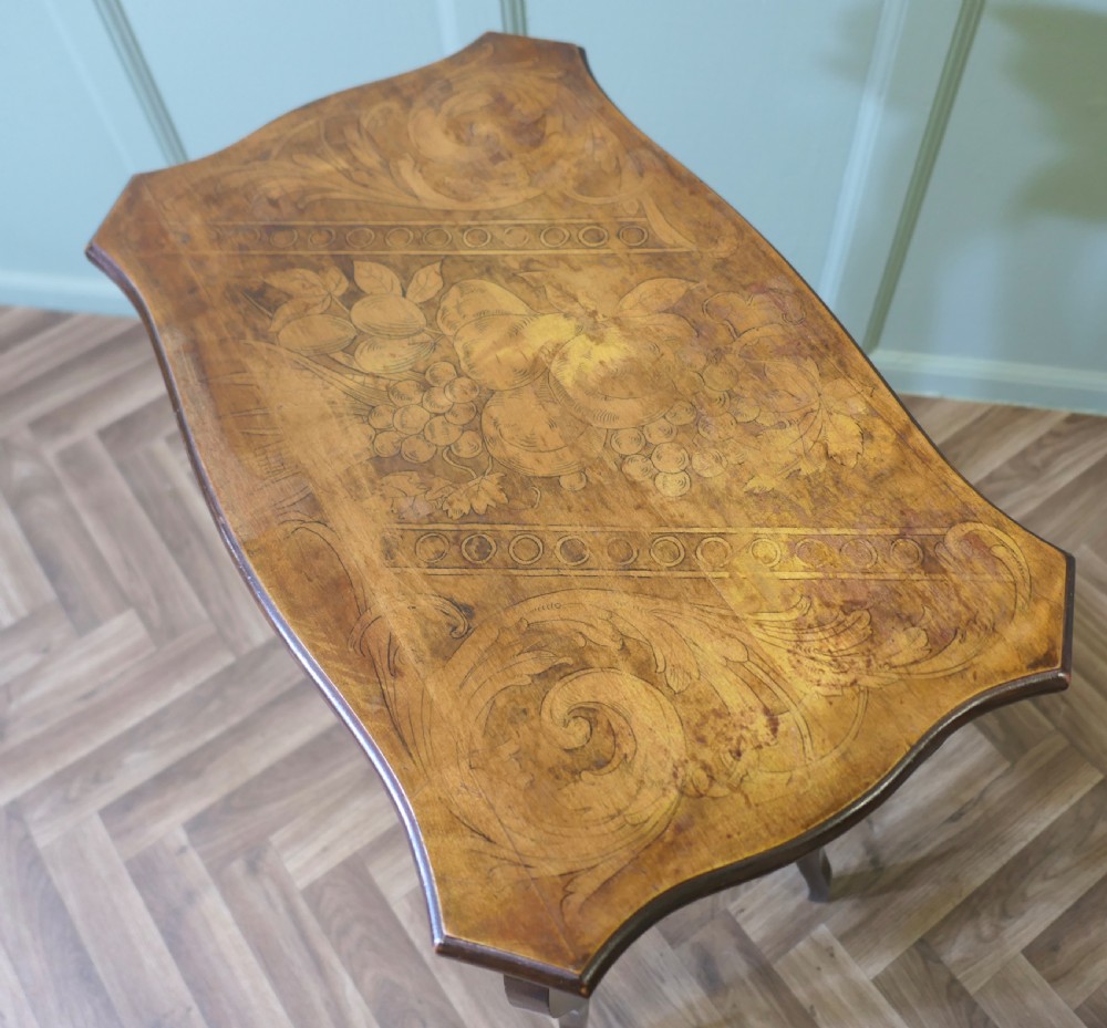 A warm brown wooden occasional table featuring a shaped serpentine top with central floral decoration, slender cabriole legs, and a decorated lower shelf. View VI