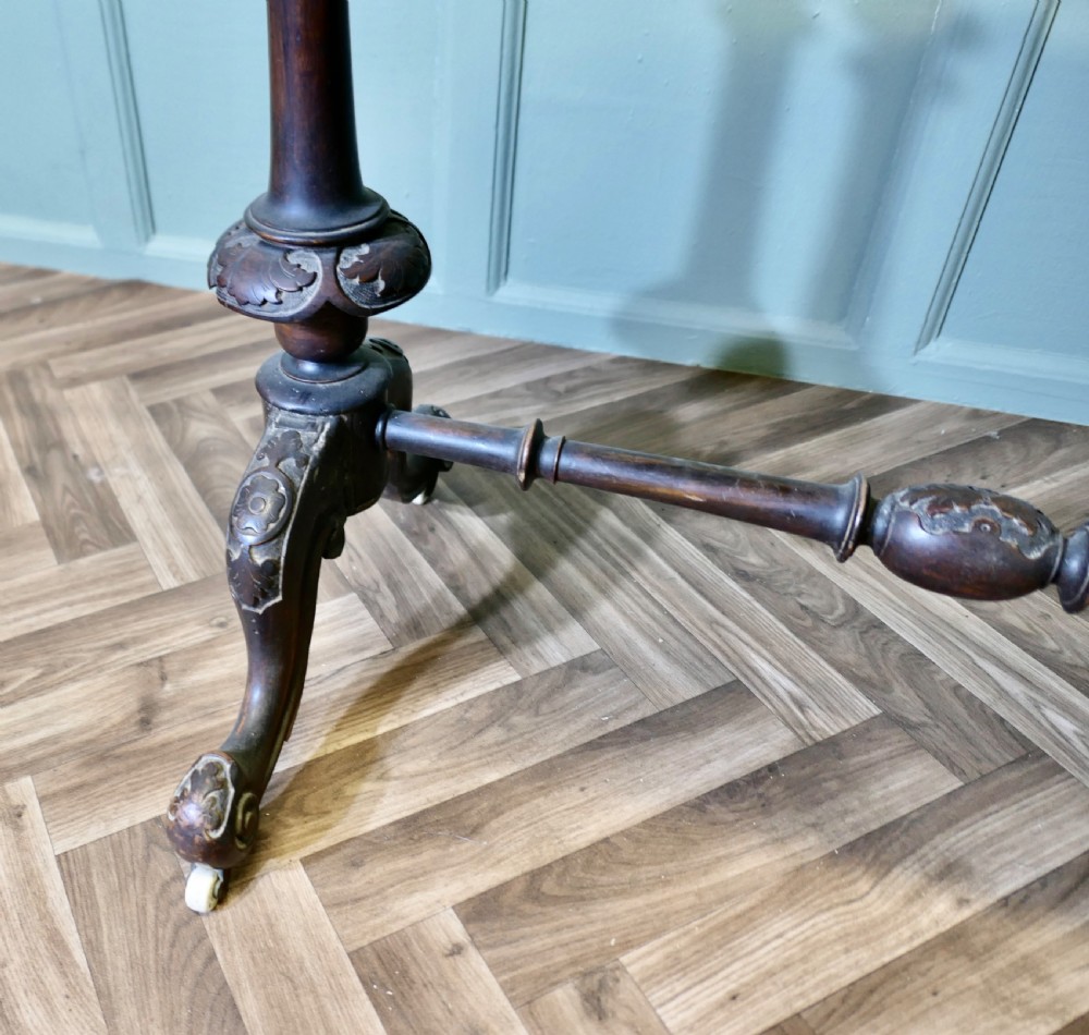 A Victorian oval walnut centre table featuring a polished timber top, turned support columns, a central stretcher, and carved legs with white ceramic castors. View III