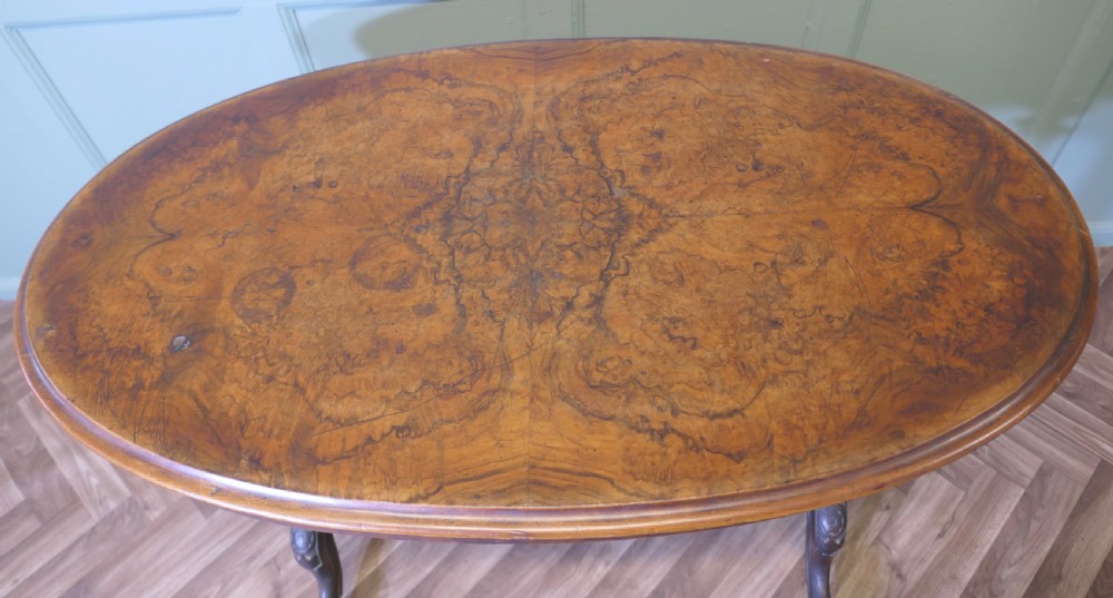 A Victorian oval walnut centre table featuring a polished timber top, turned support columns, a central stretcher, and carved legs with white ceramic castors. View V