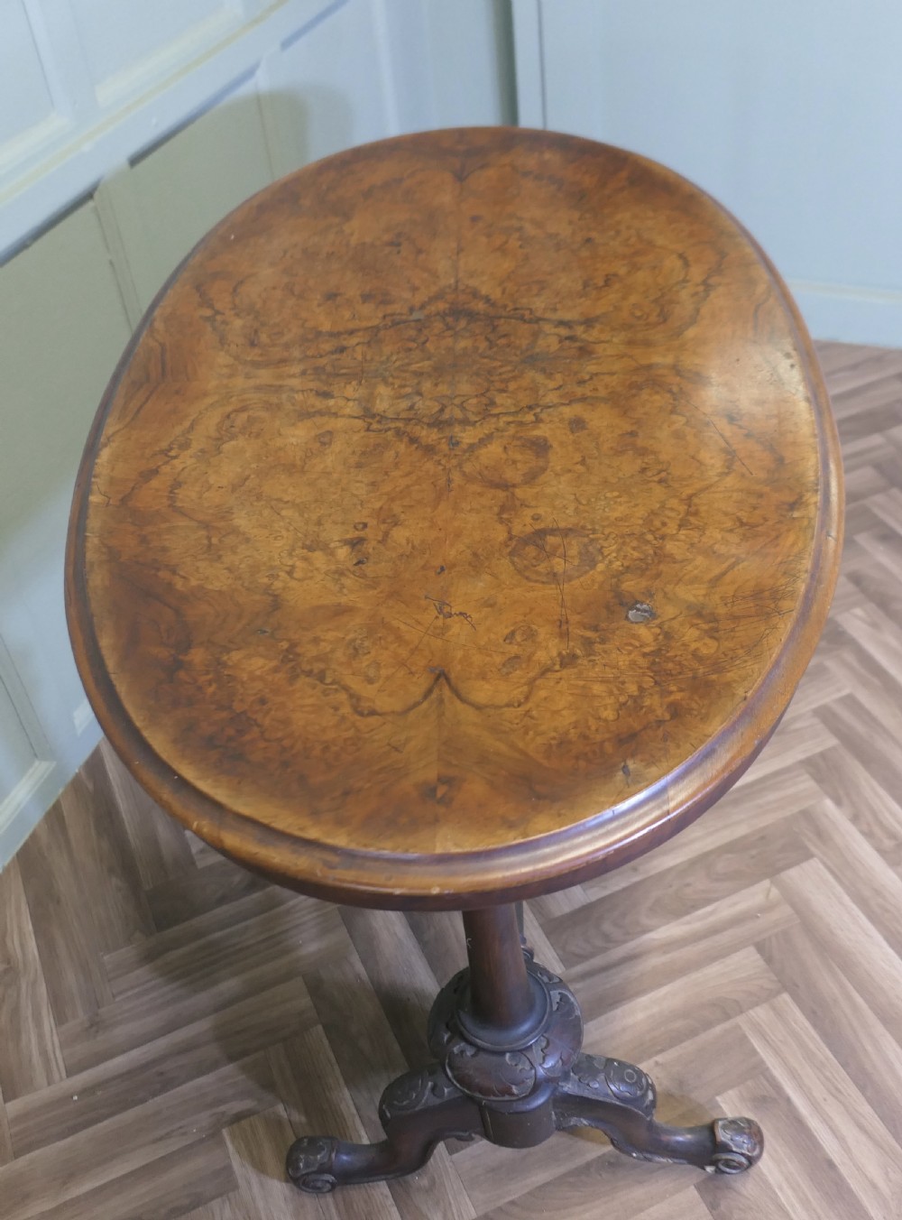 A Victorian oval walnut centre table featuring a polished timber top, turned support columns, a central stretcher, and carved legs with white ceramic castors. View VI