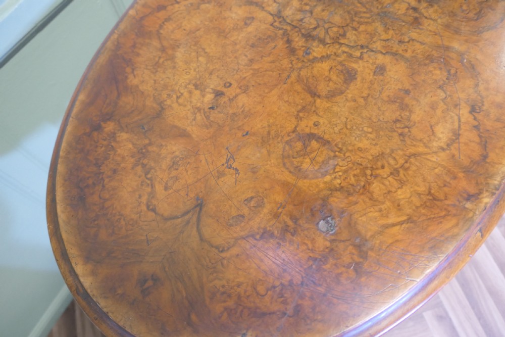 A Victorian oval walnut centre table featuring a polished timber top, turned support columns, a central stretcher, and carved legs with white ceramic castors. View VII