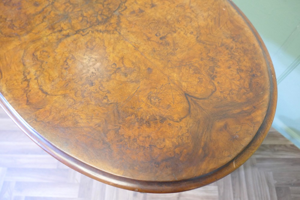 A Victorian oval walnut centre table featuring a polished timber top, turned support columns, a central stretcher, and carved legs with white ceramic castors. View VIII