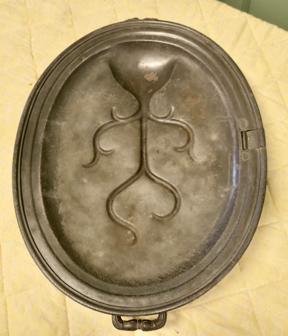 An oval antique pewter meat platter featuring raised tree-like drainage channels leading to a well at one end, flanked by a moulded rim.