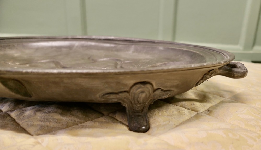 An oval antique pewter meat platter featuring raised tree-like drainage channels leading to a well at one end, flanked by a moulded rim. View V