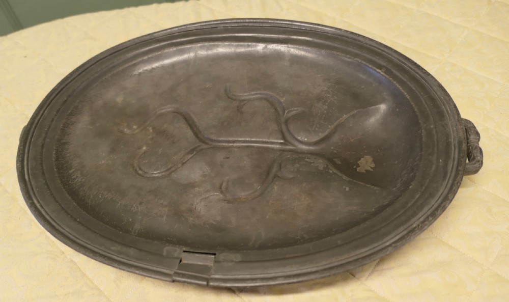 An oval antique pewter meat platter featuring raised tree-like drainage channels leading to a well at one end, flanked by a moulded rim. View VI