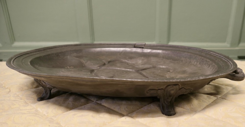 An oval antique pewter meat platter featuring raised tree-like drainage channels leading to a well at one end, flanked by a moulded rim. View VII