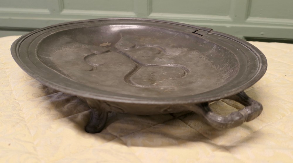 An oval antique pewter meat platter featuring raised tree-like drainage channels leading to a well at one end, flanked by a moulded rim. View IX
