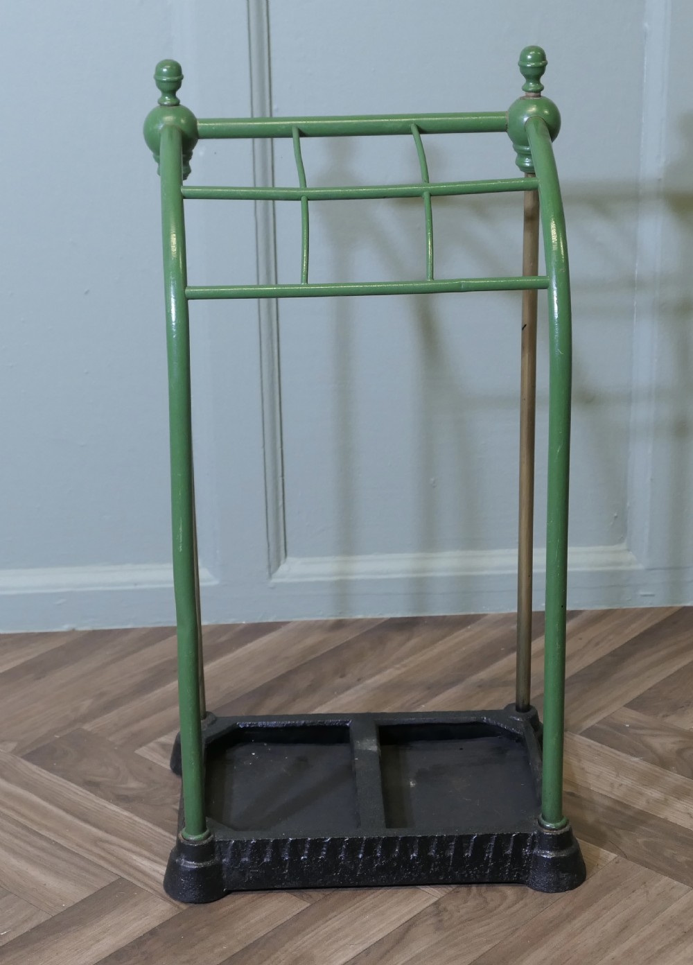 A Victorian umbrella stand featuring a green painted tubular frame with finials, brass support rods, divided upper sections, and a heavy black cast iron drip tray base. View II