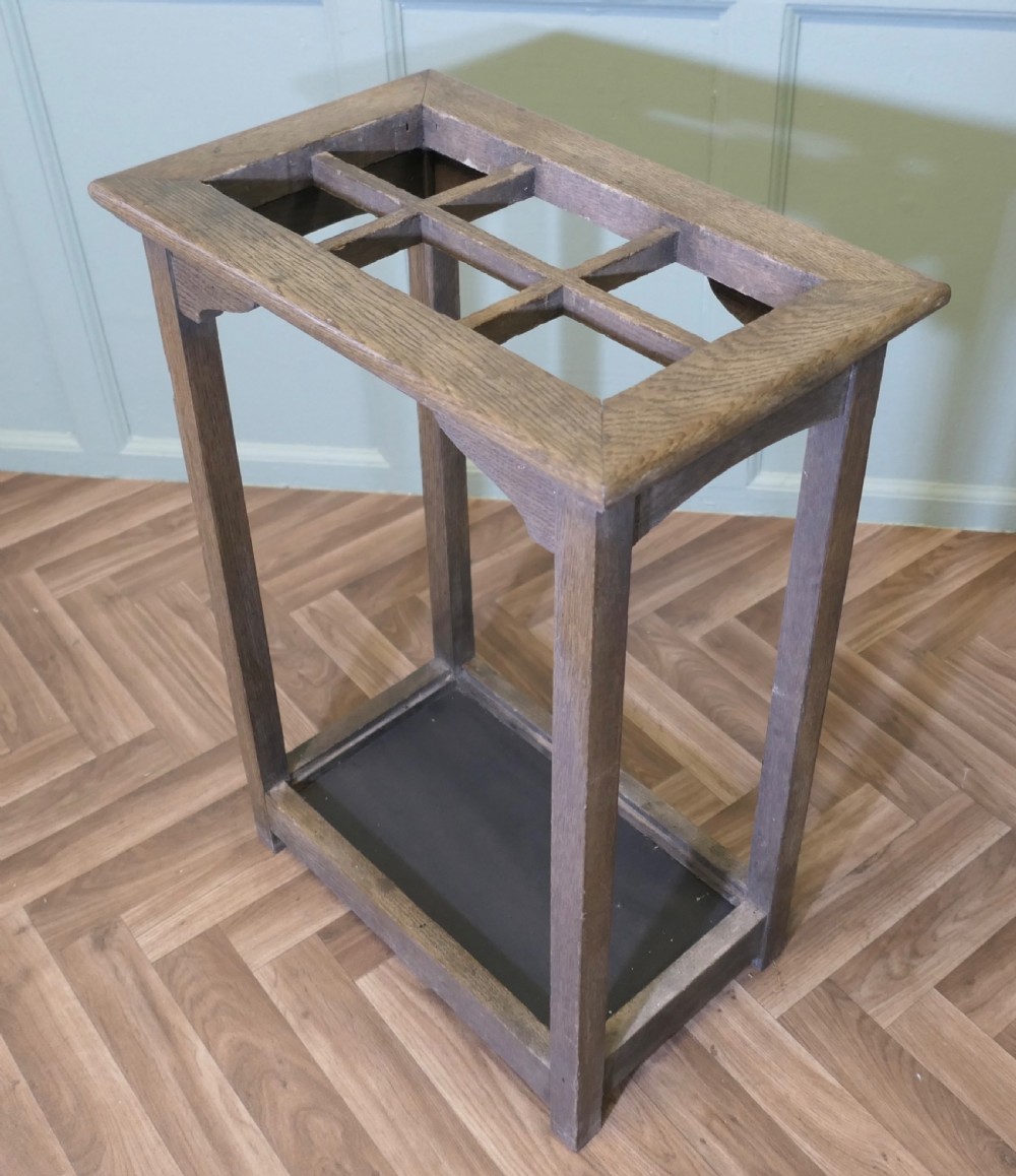 A rectangular Arts and Crafts oak umbrella stand featuring a six-compartment top grid, four square legs with corner brackets, and a dark base tray. View III