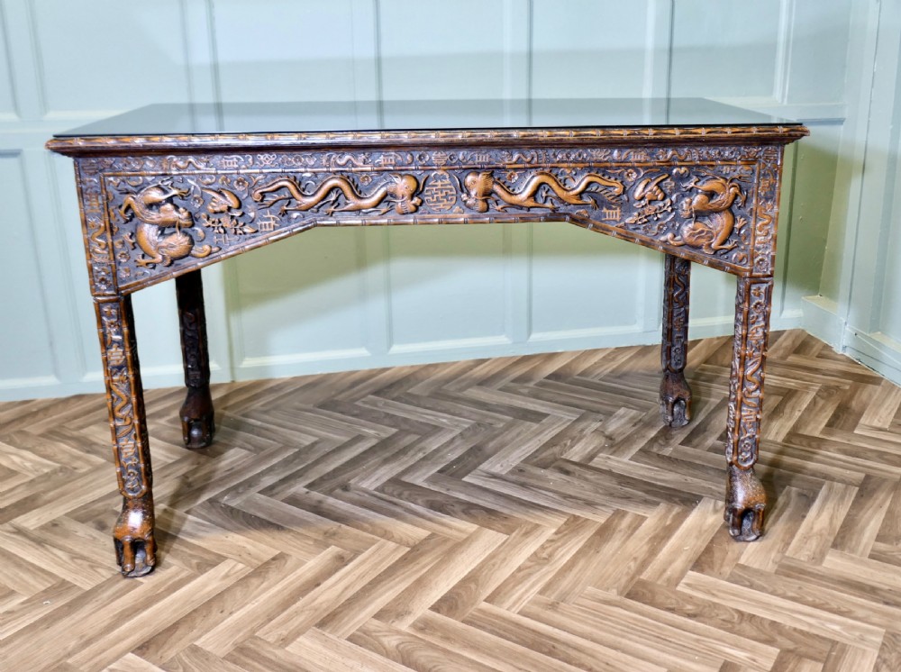 A dark brown carved wood console table featuring relief dragons on the frieze and legs with a fitted glass top.