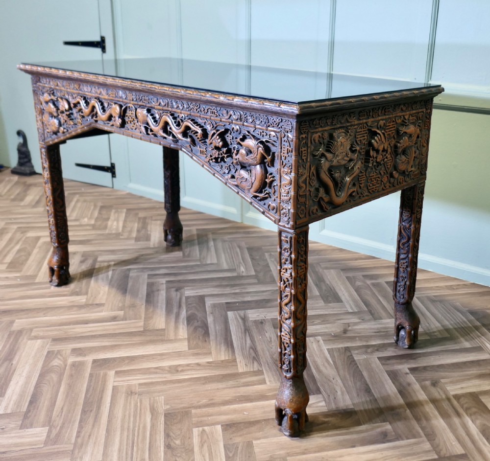 A dark brown carved wood console table featuring relief dragons on the frieze and legs with a fitted glass top. View II