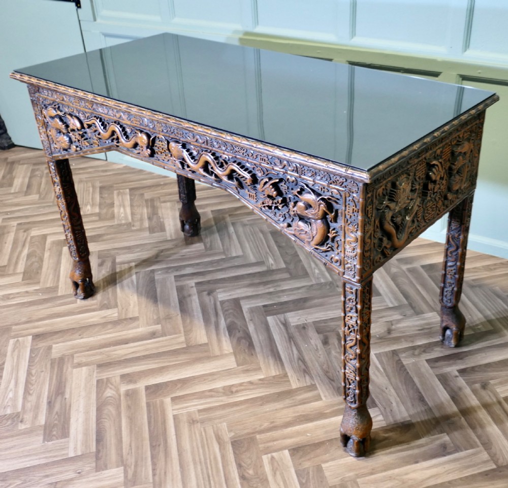 A dark brown carved wood console table featuring relief dragons on the frieze and legs with a fitted glass top. View V