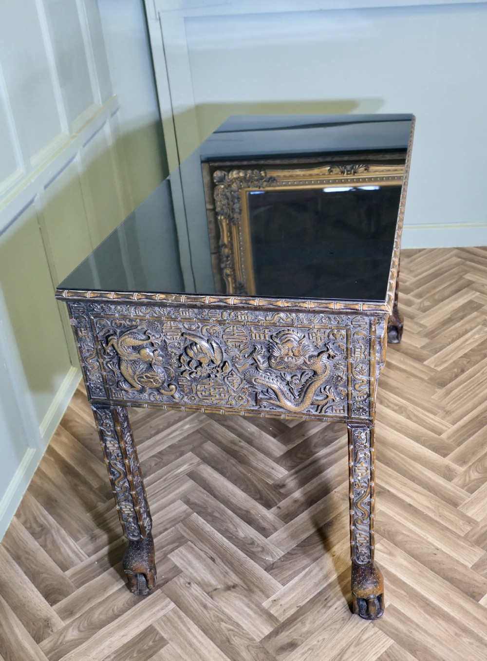A dark brown carved wood console table featuring relief dragons on the frieze and legs with a fitted glass top. View VI