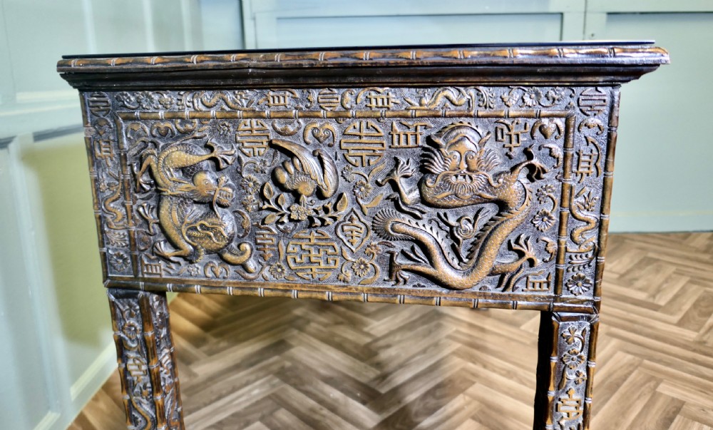 A dark brown carved wood console table featuring relief dragons on the frieze and legs with a fitted glass top. View VII
