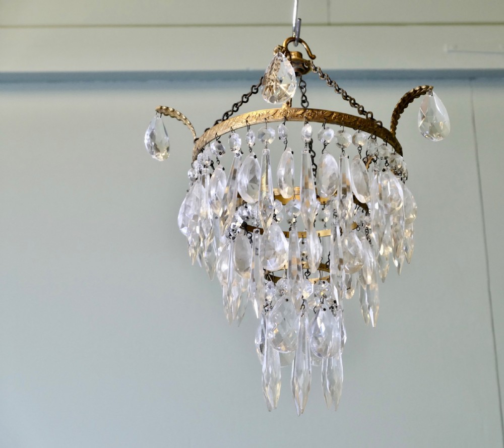 A three-tier waterfall chandelier featuring faceted glass drops suspended from an embossed brass ring with extended scroll arms. View V
