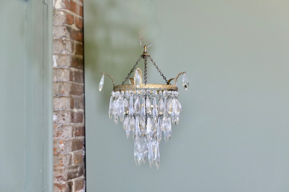 A three-tier waterfall chandelier featuring faceted glass drops suspended from an embossed brass ring with extended scroll arms. View VI