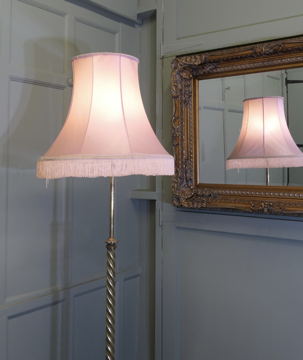 An antique brass floor lamp with a twisted column stem, adjustable height section, and a pink fabric shade with tassel fringe.