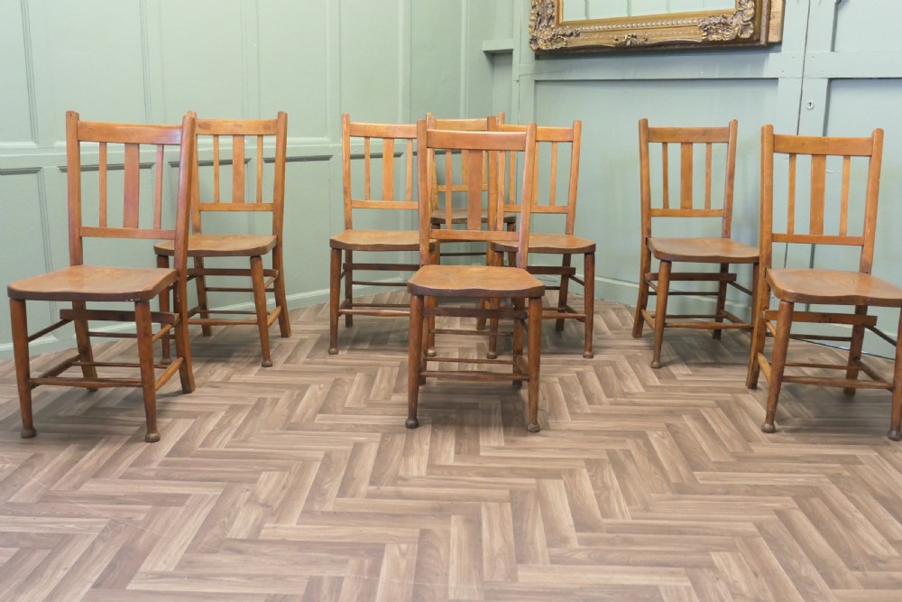 A set of eight Victorian beech and elm school chairs featuring vertical slat backs, shaped wooden seats, and turned legs with stretchers.