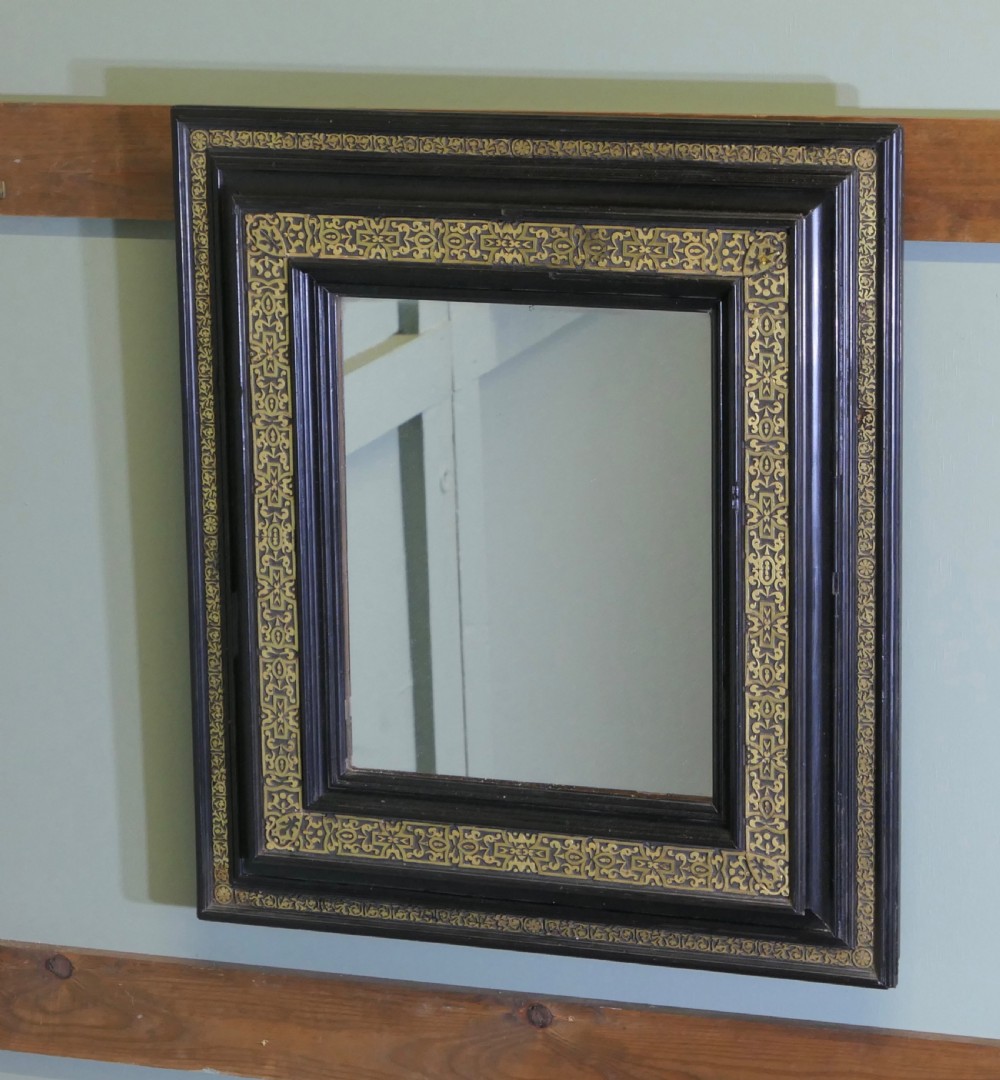 A rectangular black ebonised wall mirror featuring ornate gilt brass chased mounts along its frame.