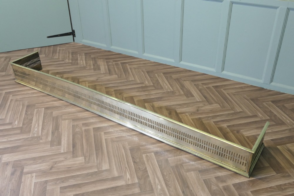 A long 19th-century brass fireplace fender featuring two rows of vertical pierced fretwork slots along its front panel.