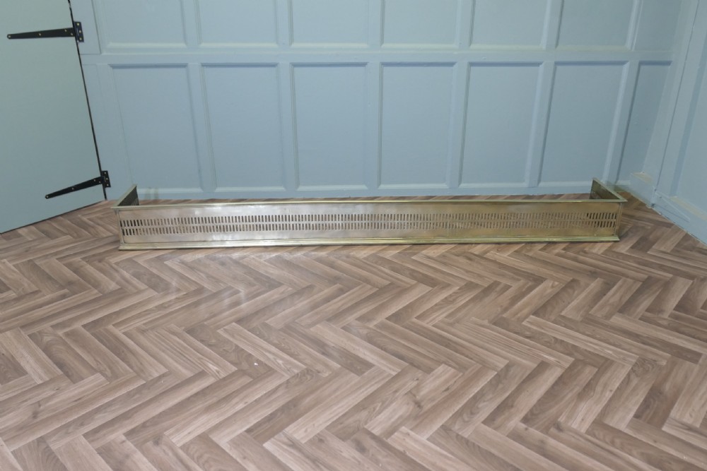 A long 19th-century brass fireplace fender featuring two rows of vertical pierced fretwork slots along its front panel. View VII