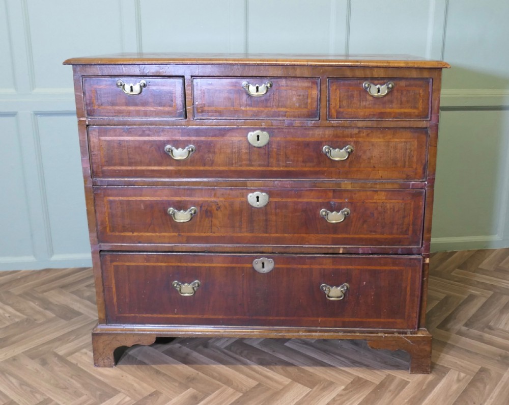 An 18th-century chest of drawers featuring inlaid walnut and satinwood crossbanding with brass drop handles and bracket feet.