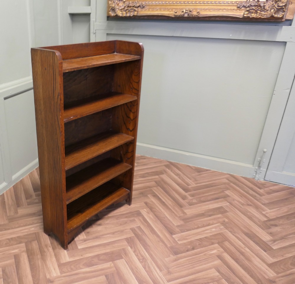 A medium brown freestanding oak open bookcase featuring four fixed shelves, a rounded top gallery, and a shaped apron base. View III