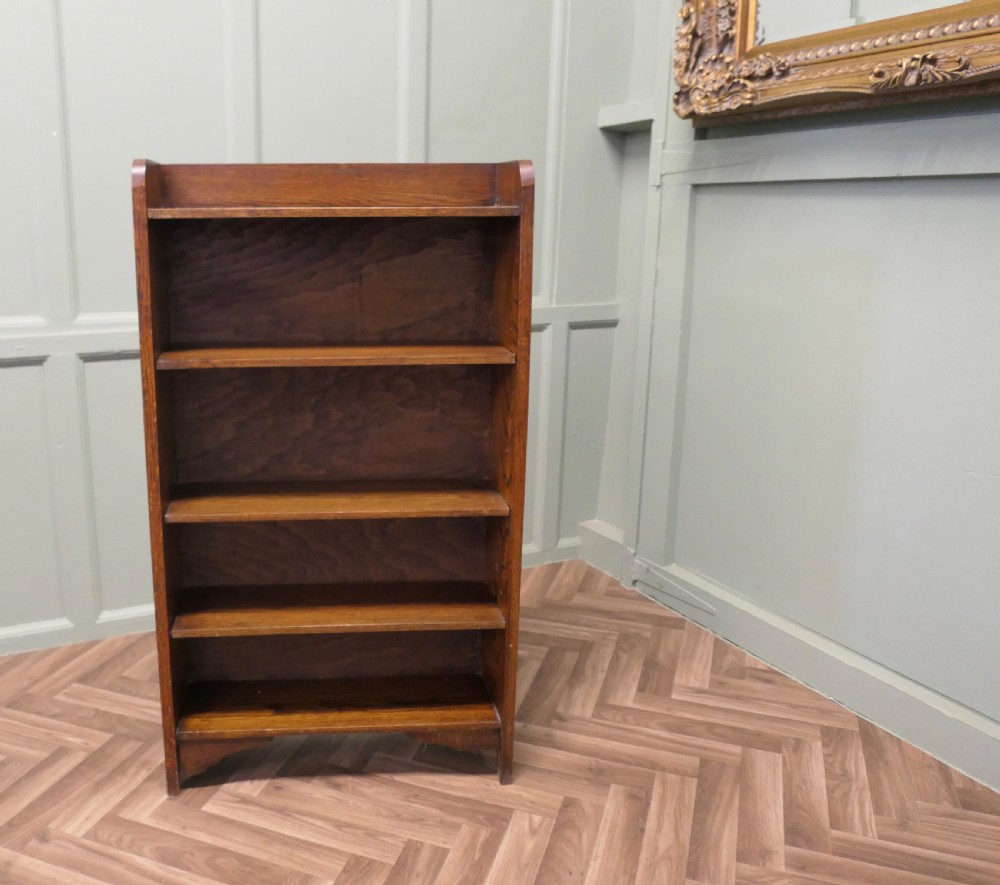 A medium brown freestanding oak open bookcase featuring four fixed shelves, a rounded top gallery, and a shaped apron base. View V