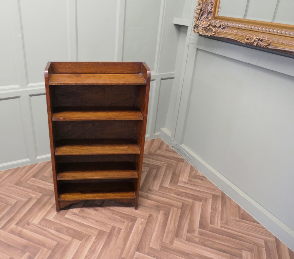 A medium brown freestanding oak open bookcase featuring four fixed shelves, a rounded top gallery, and a shaped apron base. View VI