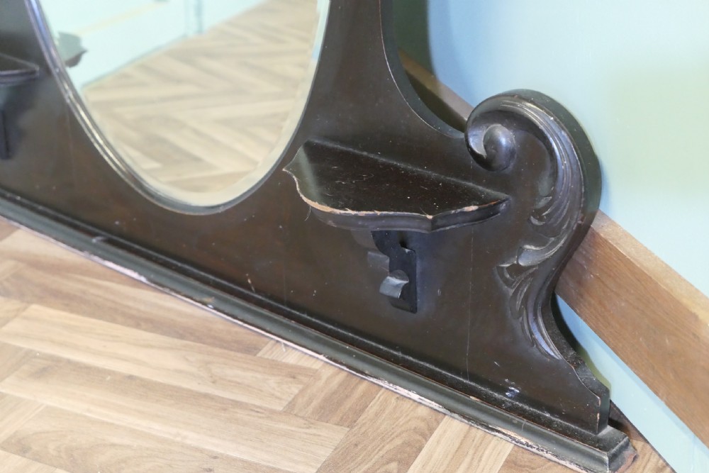 An Edwardian black lacquered overmantel mirror featuring a central heart-shaped glass plate, carved leaf crest, and two integrated side display shelves. View II
