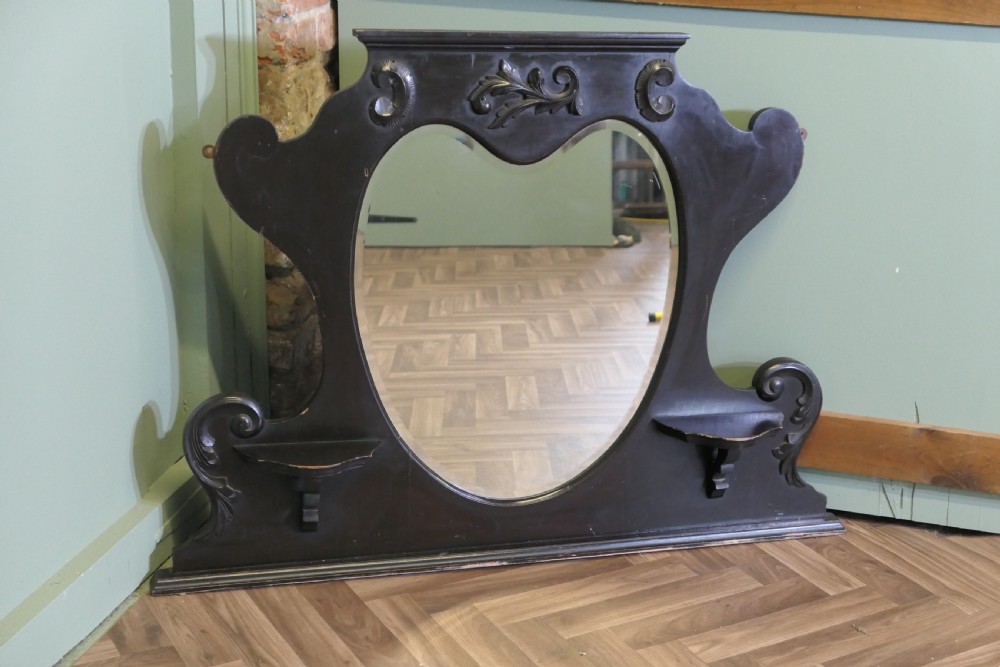 An Edwardian black lacquered overmantel mirror featuring a central heart-shaped glass plate, carved leaf crest, and two integrated side display shelves. View III