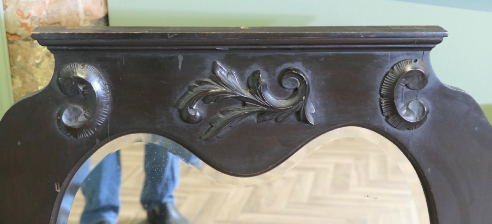 An Edwardian black lacquered overmantel mirror featuring a central heart-shaped glass plate, carved leaf crest, and two integrated side display shelves. View V
