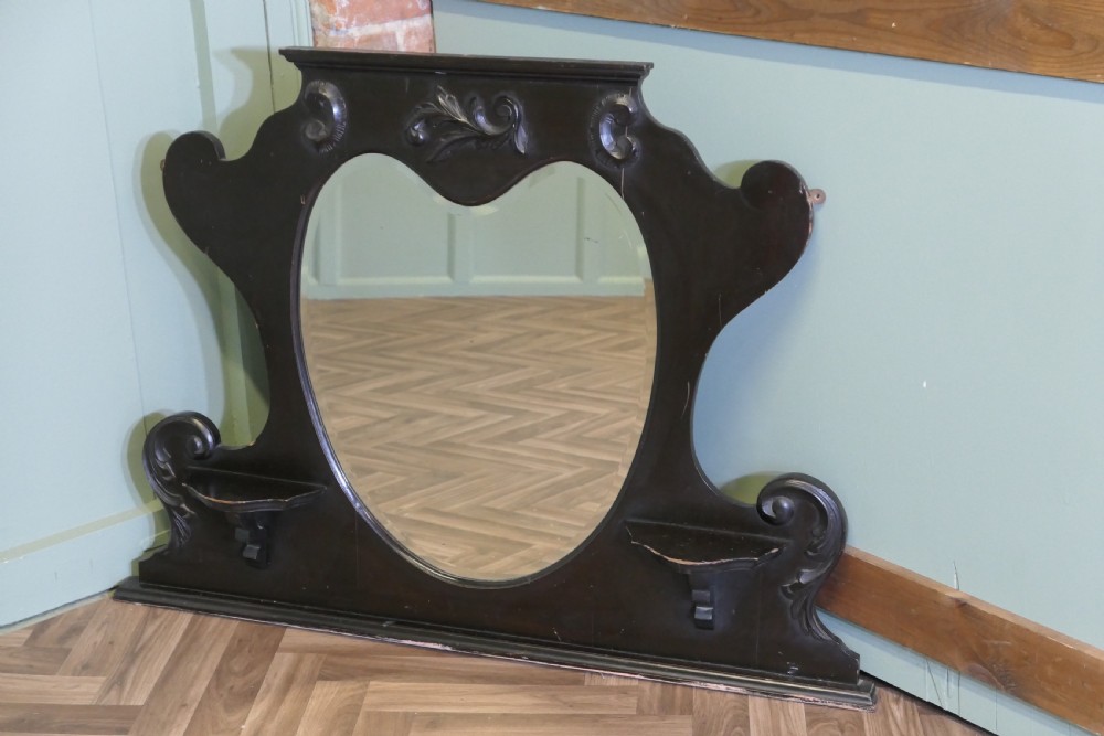 An Edwardian black lacquered overmantel mirror featuring a central heart-shaped glass plate, carved leaf crest, and two integrated side display shelves. View VI